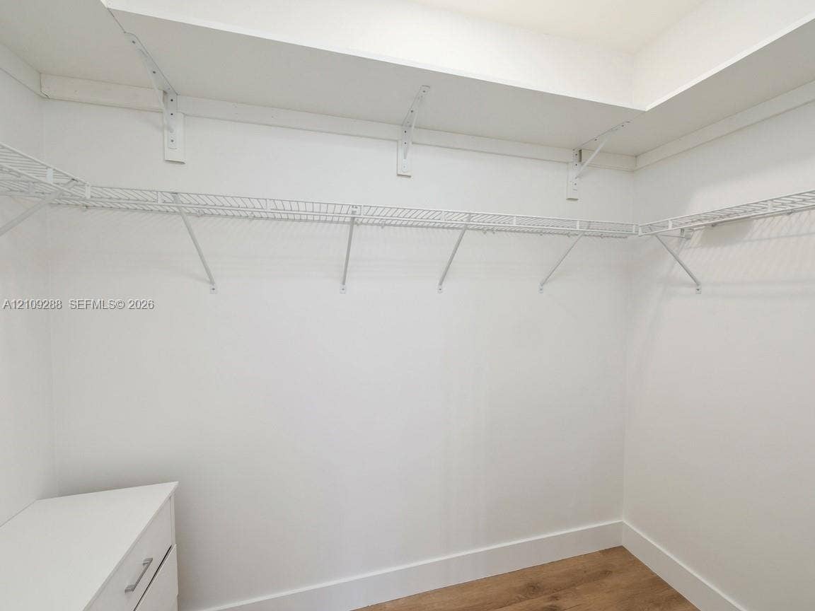 Walk-in storage space featuring built-in white shelving and wood-finish flooring