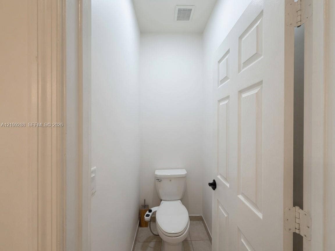 Enclosed space featuring a six-panel door with matte black hardware, tile flooring, and a porcelain toilet with an integrated bidet attachment