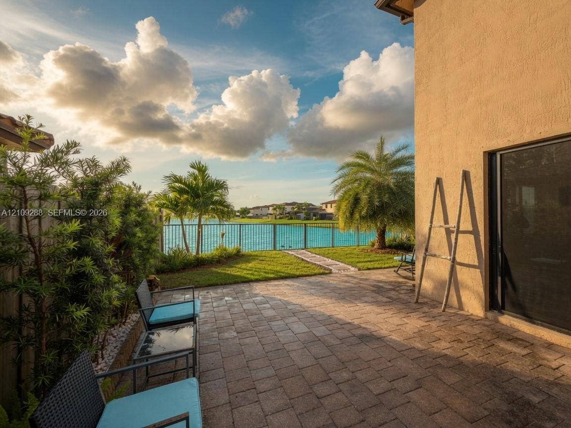 Paver patio featuring a manicured lawn, metal perimeter fencing, and water frontage