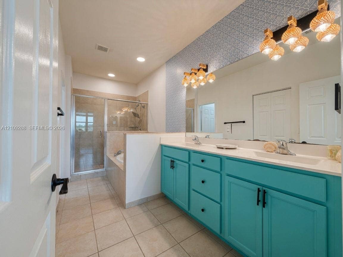 Double vanity with bright cabinetry, light-toned countertop, dual integrated sinks, extensive wall-to-wall mirror, and a glass-enclosed shower with tile surround