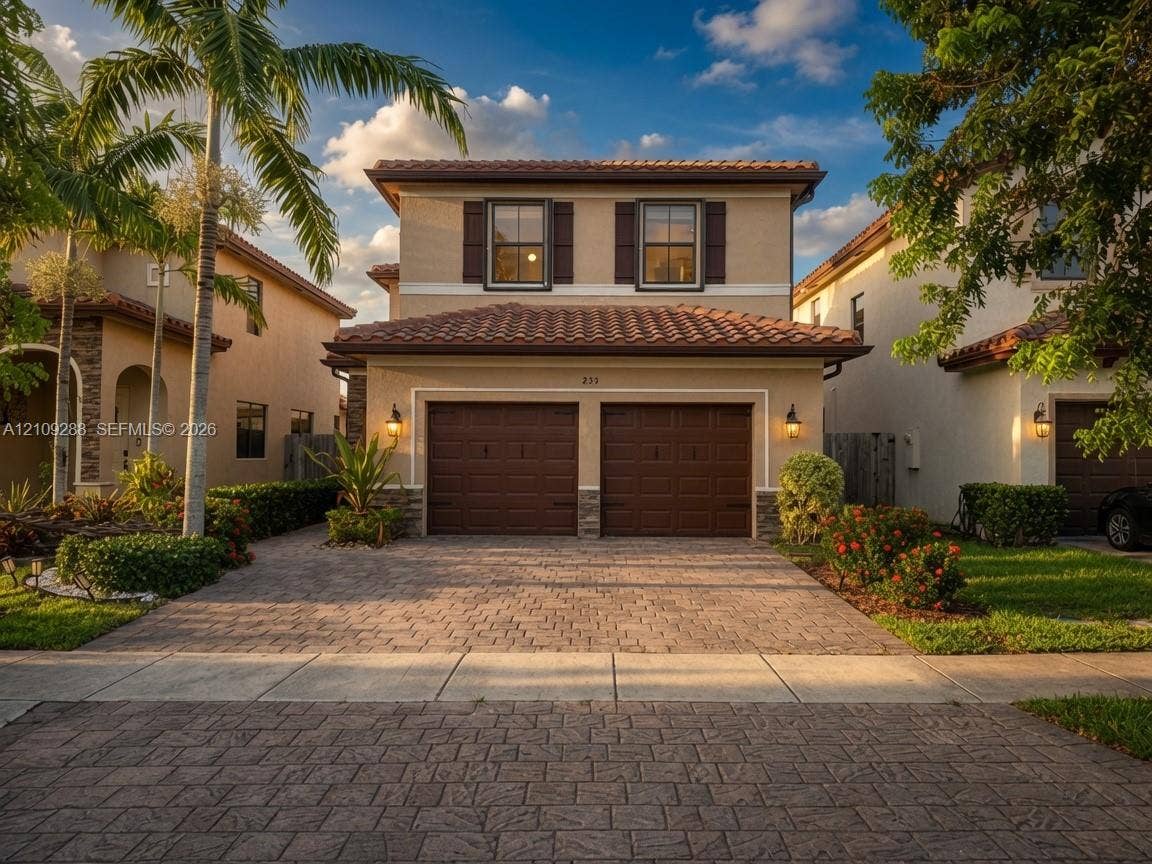 Two-story residence featuring a tile roof, stucco exterior, two-car garage, and paver driveway with integrated landscaping