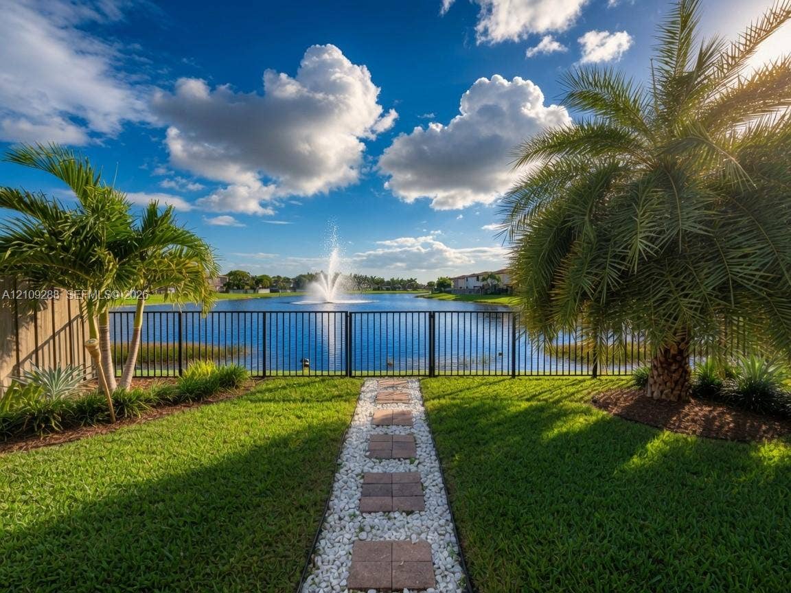 Backyard featuring a paver and gravel walkway, metal fencing, and palm landscaping