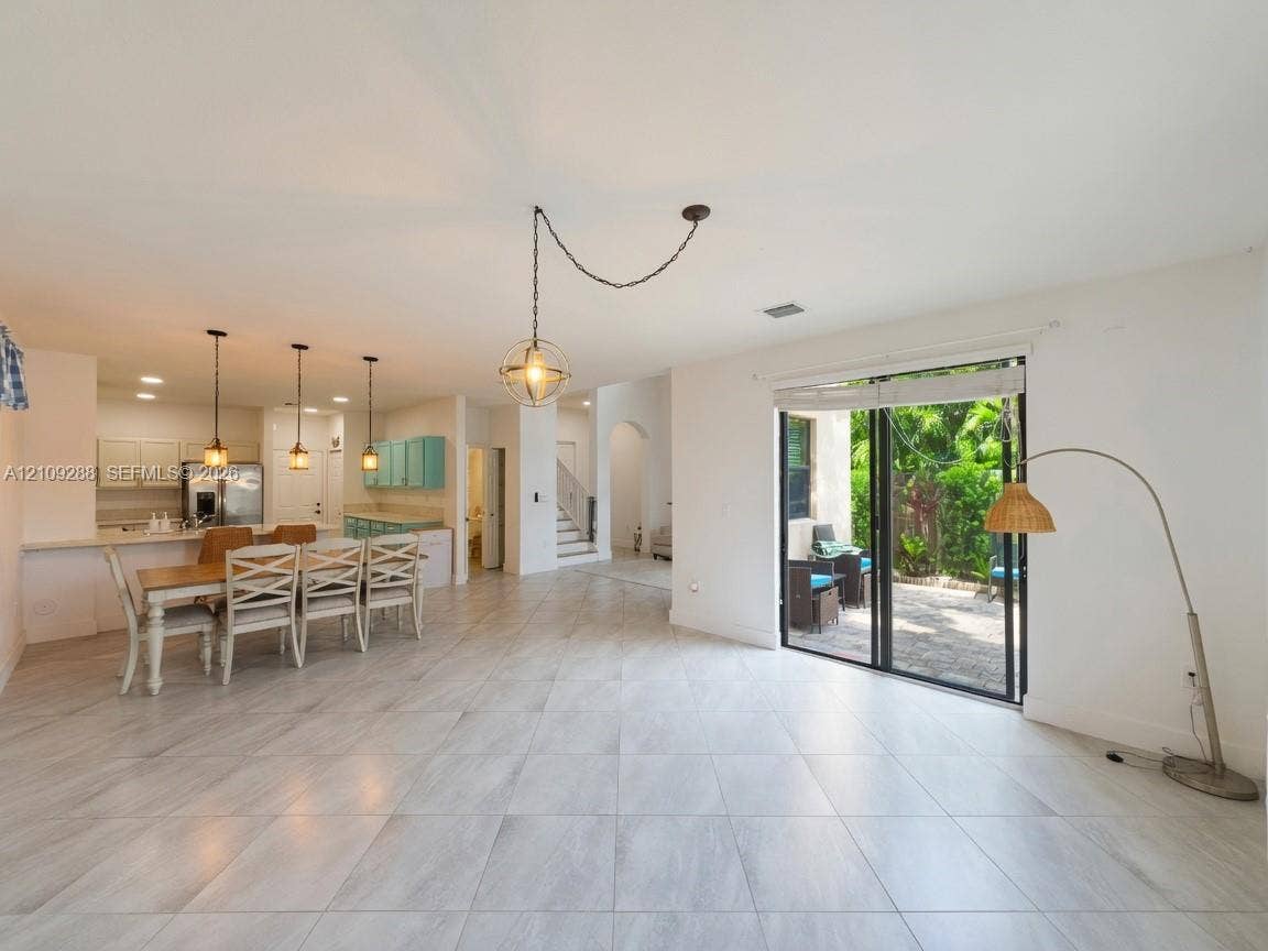 Open-concept interior featuring large-format tile flooring, recessed lighting, triple pendant fixtures, and sliding glass doors to a stone-paved patio