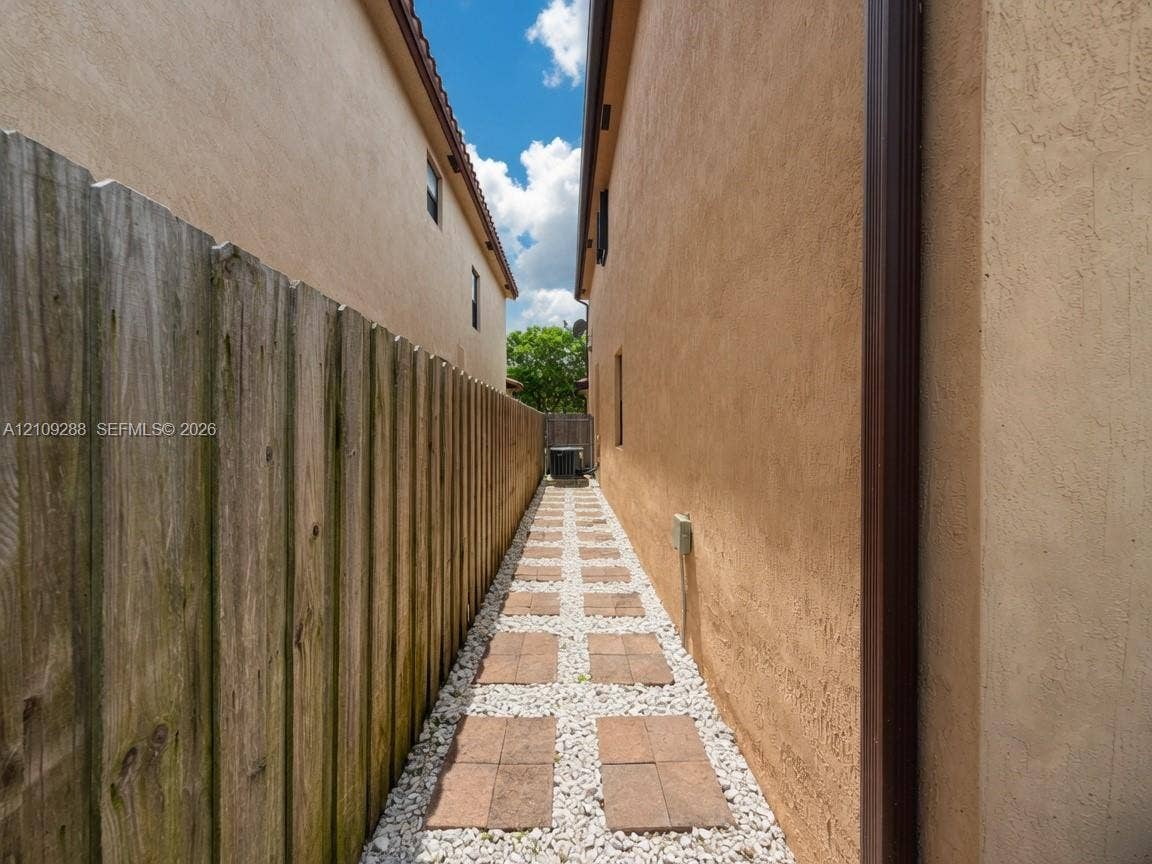 Side yard featuring stucco exterior walls, a vertical wood privacy fence, and a stone-inlaid paver walkway