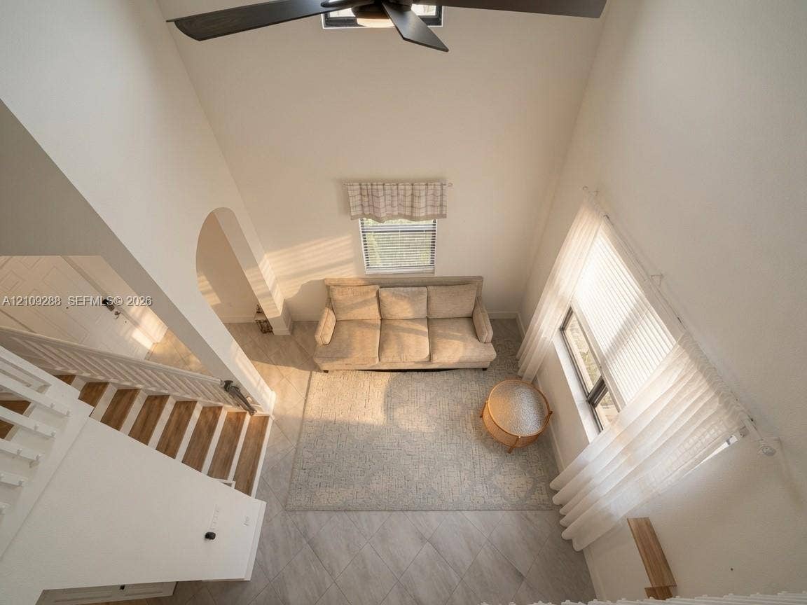 Vaulted ceiling featuring a central multi-blade ceiling fan, neutral tile flooring, arched entryway, and tall windows