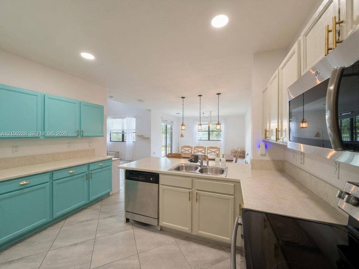 Kitchen featuring dual-tone cabinetry, stone-finish countertops, stainless steel appliances, large central island, and tile flooring