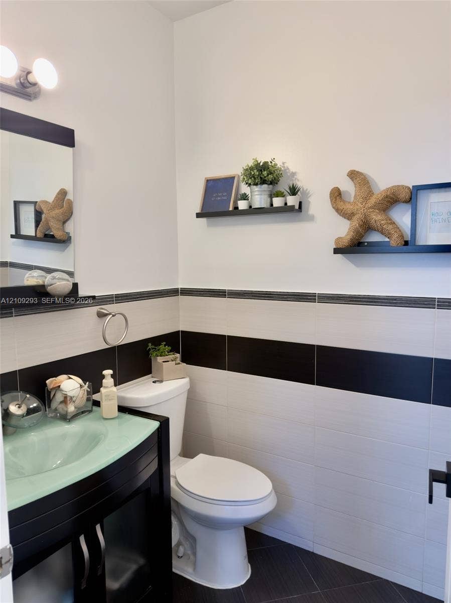 8880 NW 115th Court, Doral, FL 33178 Vanity featuring a green glass vessel sink and dark finish cabinetry, complemented by wall-mounted shelving and dual-tone horizontal tile wainscoting