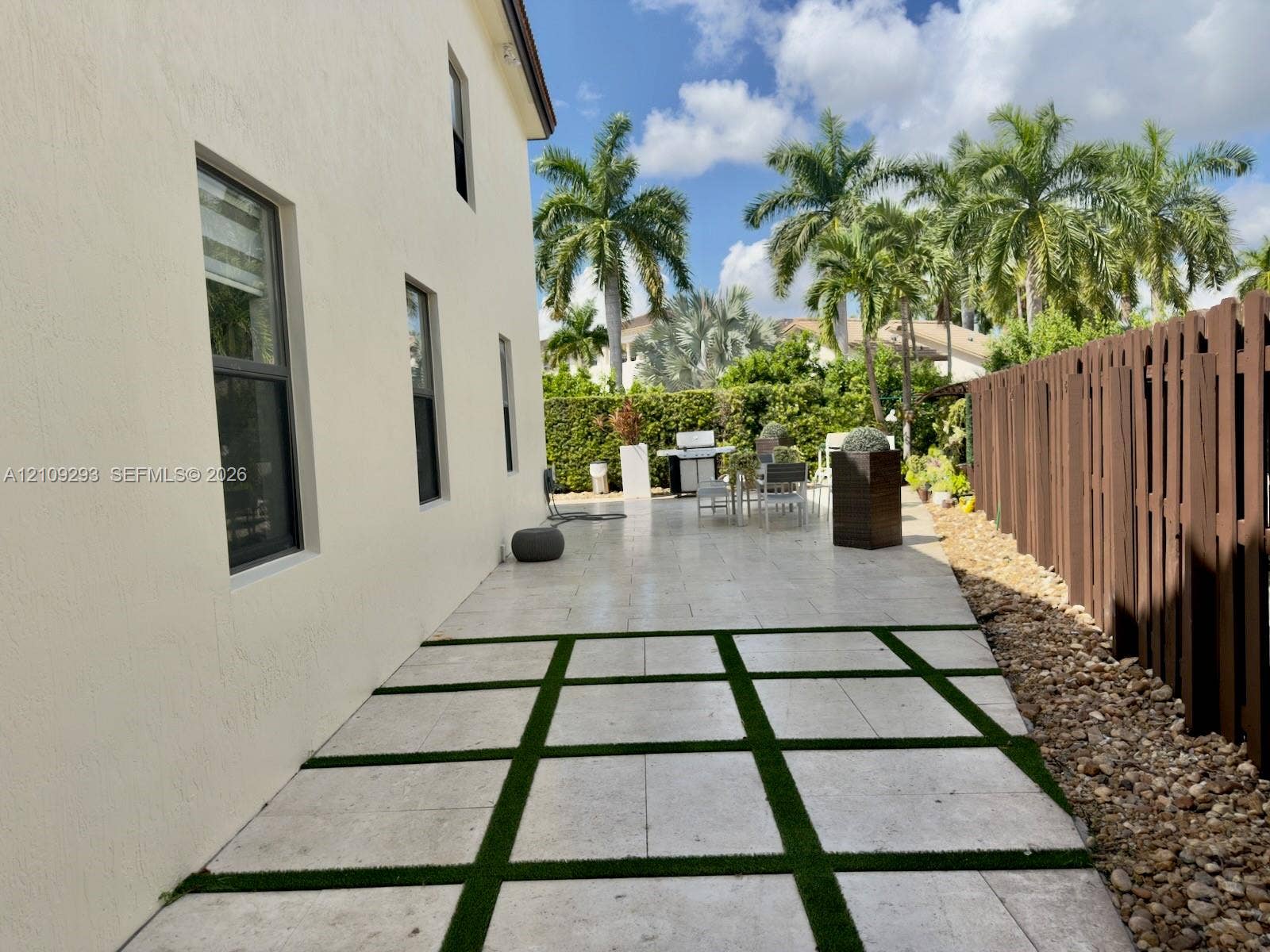 8880 NW 115th Court, Doral, FL 33178 Outdoor patio featuring large-format light-toned pavers with integrated turf grid, perimeter privacy fencing, and exterior stucco siding