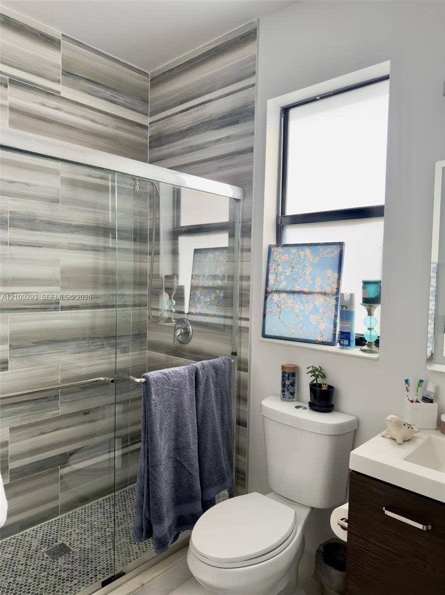 8880 NW 115th Court, Doral, FL 33178 Walk-in shower featuring floor-to-ceiling striated tile, mosaic-tiled shower floor, glass enclosure, and a wood-finish vanity with a rectangular sink and solid surface countertop
