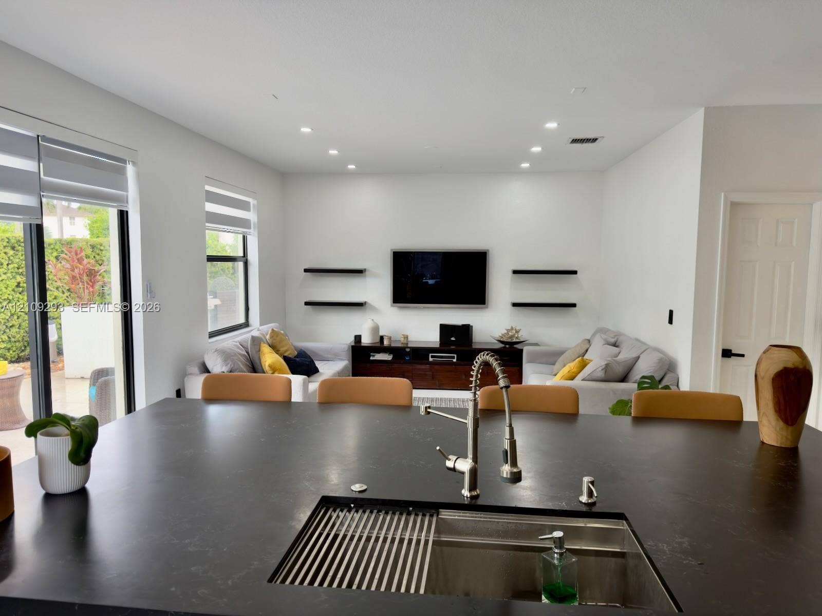 8880 NW 115th Court, Doral, FL 33178 Large kitchen island featuring a dark matte countertop, undermount stainless steel sink with a high-arch pull-down faucet, recessed ceiling lighting, and wall-mounted floating shelves
