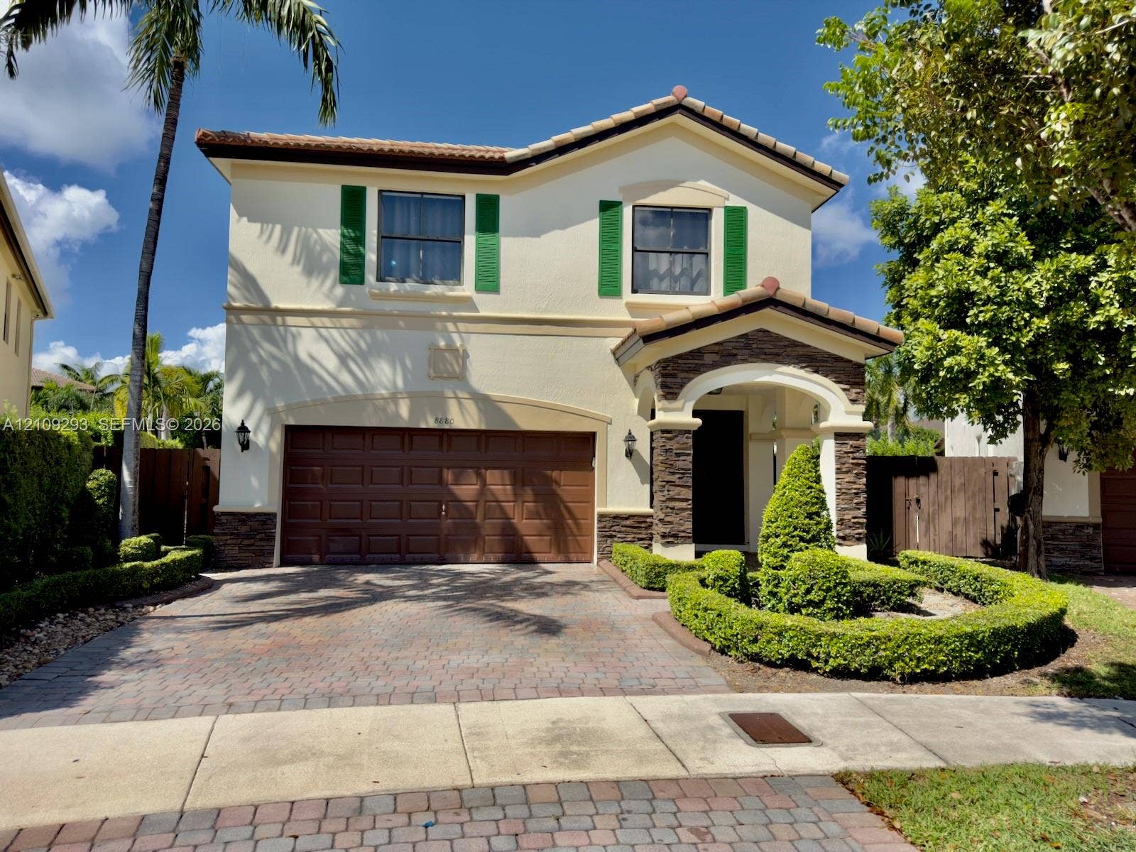 8880 NW 115th Court, Doral, FL 33178 Stucco exterior featuring decorative green shutters, stone-veneer accents, a paved driveway, and manicured landscaping
