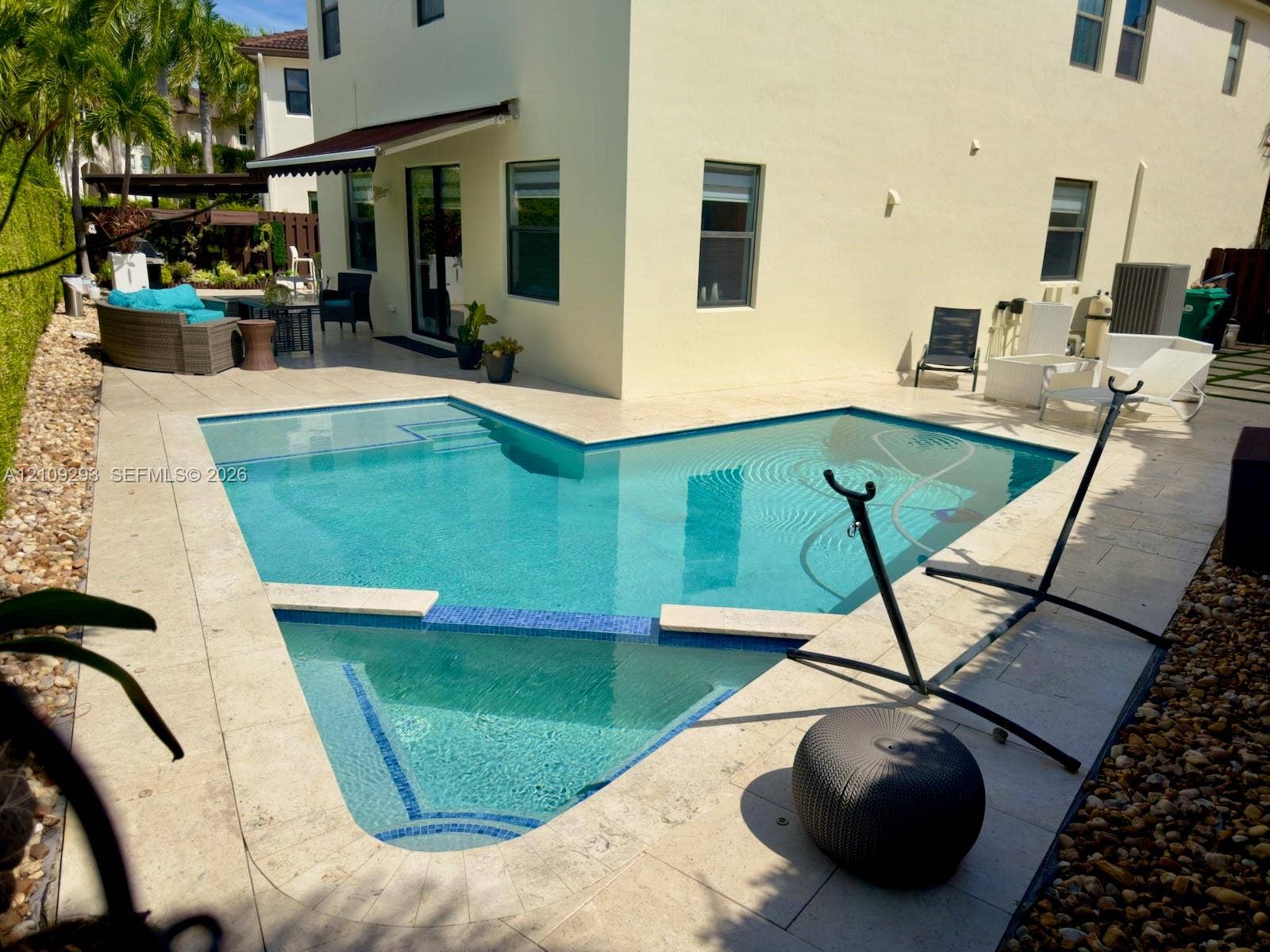 8880 NW 115th Court, Doral, FL 33178 Custom-shaped swimming pool with blue tile accents, expansive stone paver pool deck, and retractable wall-mounted awning