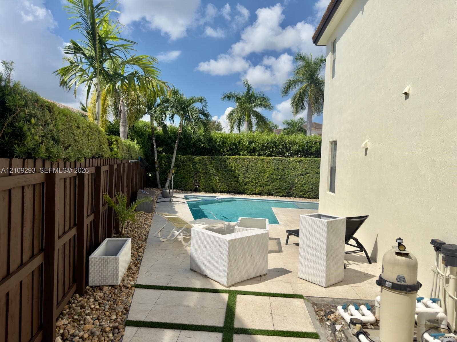 8880 NW 115th Court, Doral, FL 33178 Rear yard featuring a swimming pool, stone paver decking with integrated artificial turf accents, wood-style privacy fencing, and perimeter hedge landscaping