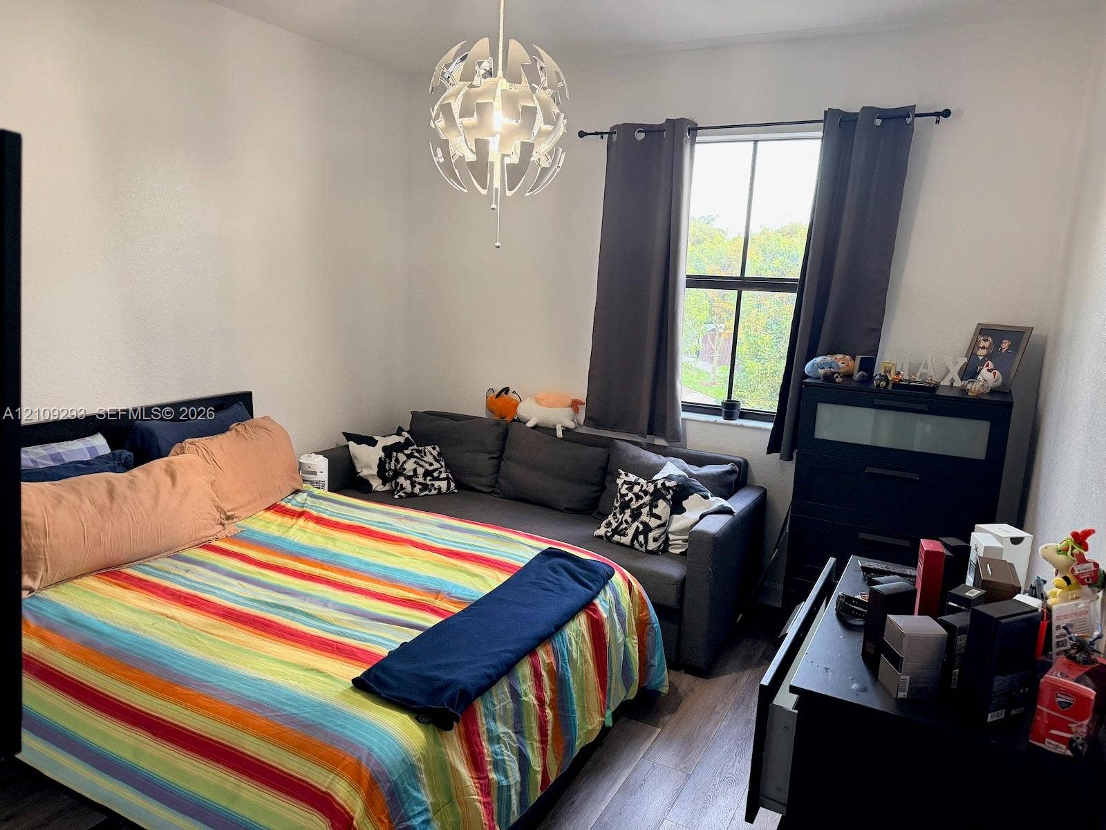 8880 NW 115th Court, Doral, FL 33178 Bedroom featuring wood-finish flooring, a multi-pane window with a black frame, and a decorative modern spherical chandelier
