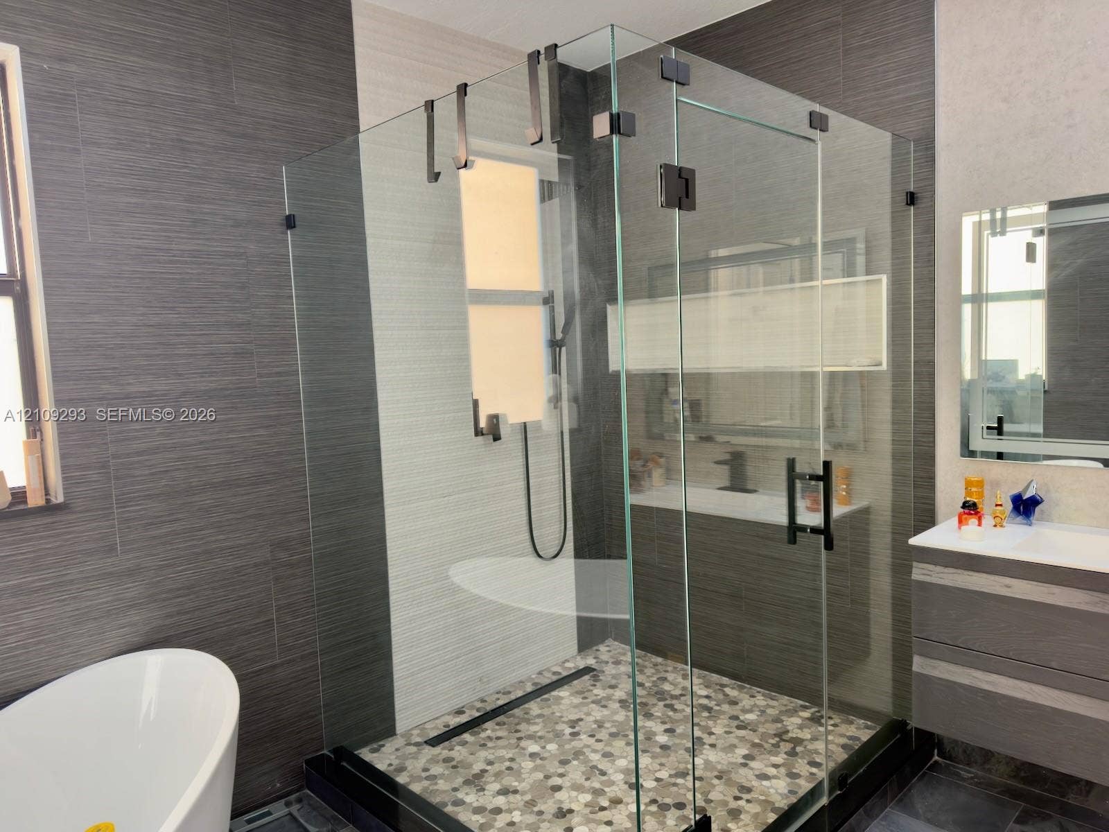 8880 NW 115th Court, Doral, FL 33178 Walk-in shower featuring a frameless glass enclosure, matte black hardware, pebble-stone flooring, and a linear drain, accompanied by a floating vanity and a freestanding soaking tub