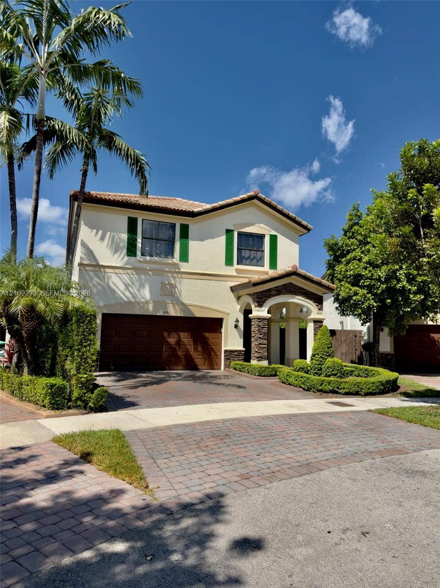 8880 NW 115th Court, Doral, FL 33178 Two-story stucco exterior with a tiled roof, stone-veneer entry columns, a multi-car garage, and a paver driveway