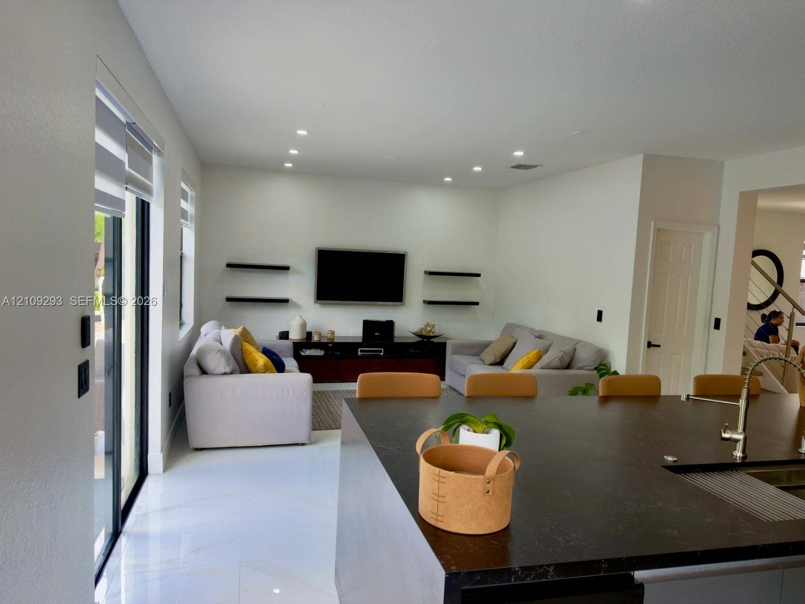 8880 NW 115th Court, Doral, FL 33178 Open-concept interior featuring large-format tile flooring, recessed ceiling lighting, a dark-toned kitchen island with a metallic faucet, and matte black floating shelving