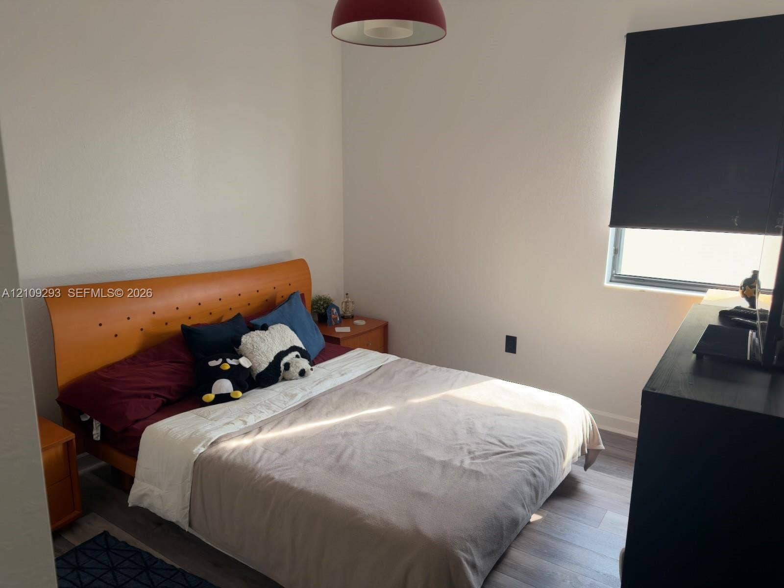 8880 NW 115th Court, Doral, FL 33178 Bright bedroom featuring warm wood-finish flooring, an upholstered platform bed with button-tufted headboard, and ample natural light from a window with blackout shade