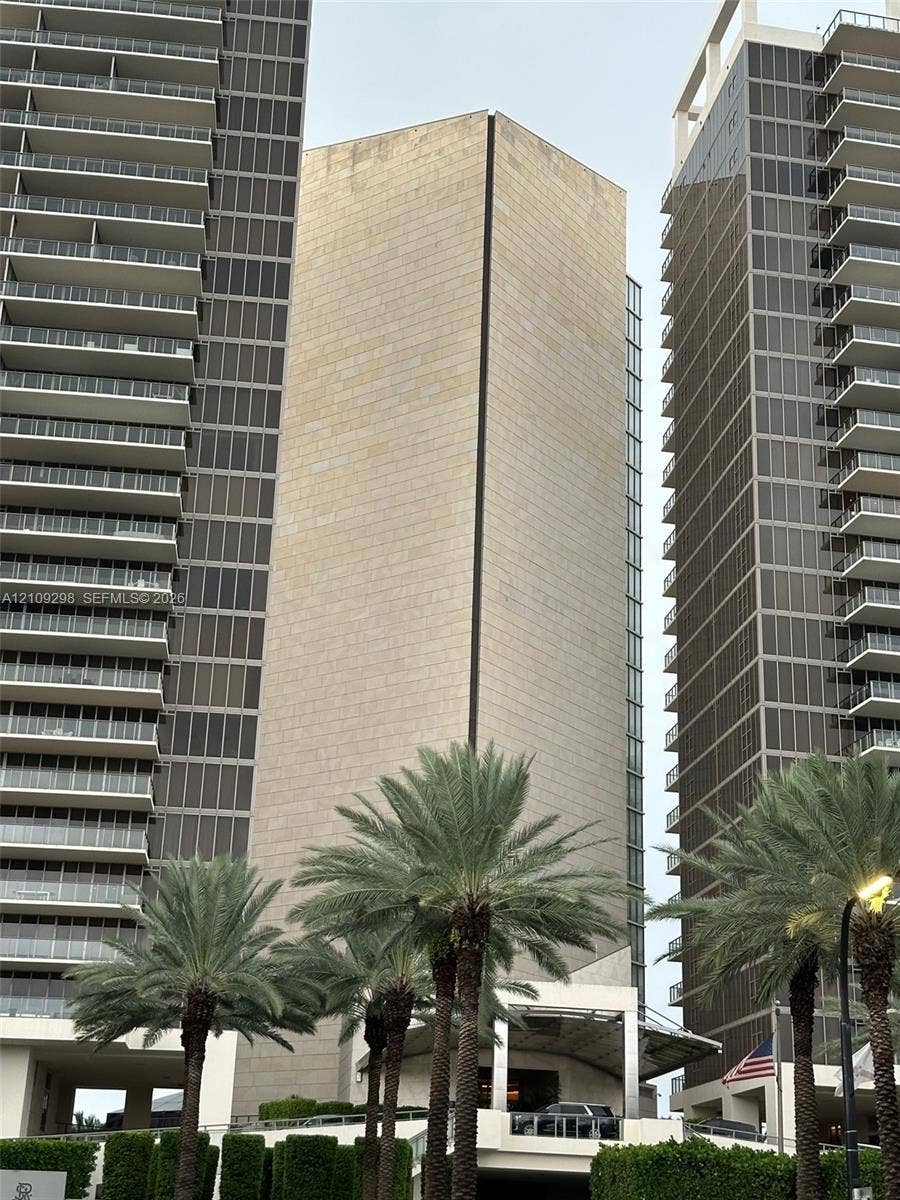 9703 Collins Avenue, #400, Bal Harbour, FL 33154 High-rise architectural exterior featuring stone cladding, multi-story glass curtain walls, and stacked private balconies, complemented by mature palm landscaping