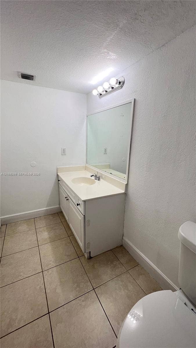 4810 NW 79 Avenue, #107, Doral, Doral, FL 33166 Bathroom featuring a white vanity cabinet, solid-surface integrated countertop with basin, wall-mounted mirror, four-light vanity fixture, and tiled flooring
