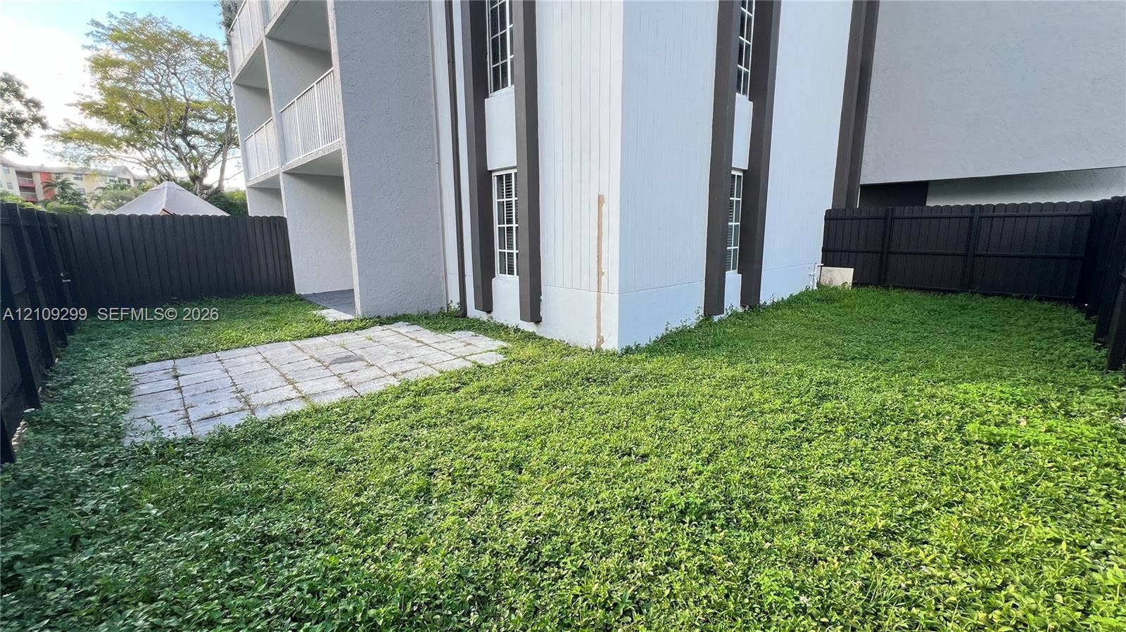 4810 NW 79 Avenue, #107, Doral, Doral, FL 33166 Private rear yard featuring a paved patio, perimeter privacy fencing, and exterior multi-story structure with grid-pane windows