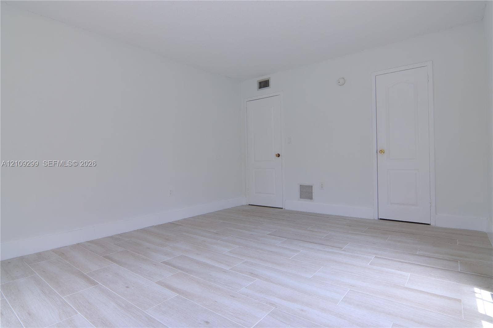 4810 NW 79 Avenue, #107, Doral, Doral, FL 33166 Neutral interior featuring wood-finish flooring, white walls, and two raised-panel doors with metallic hardware