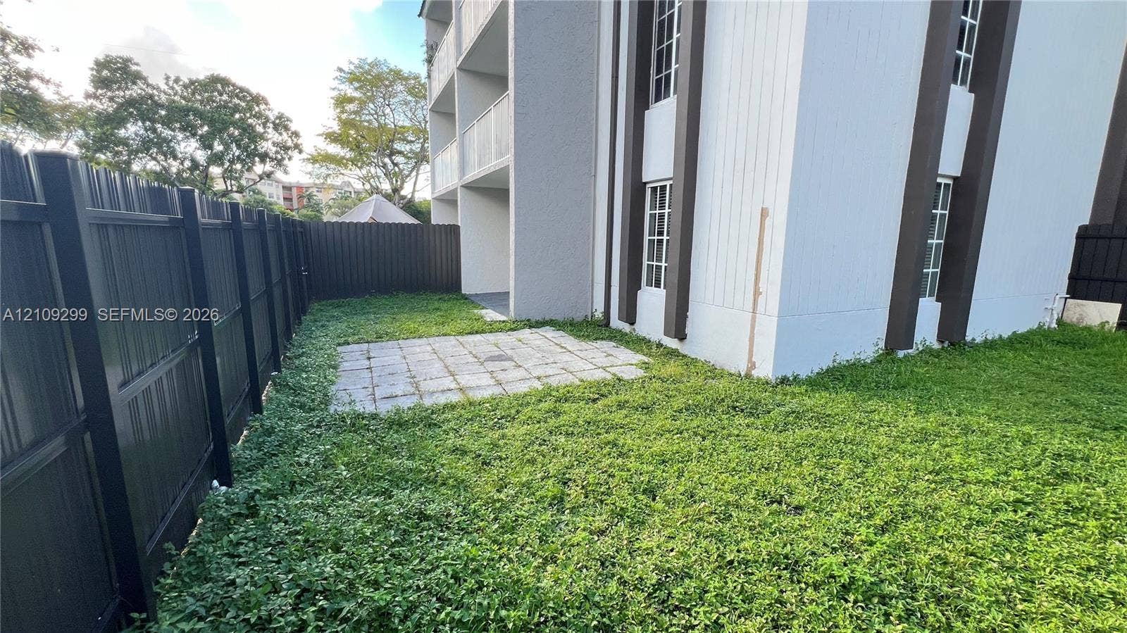 4810 NW 79 Avenue, #107, Doral, Doral, FL 33166 Ground-level patio space enclosed by a black metal privacy fence, featuring exterior siding with vertical trim accents and multi-pane windows
