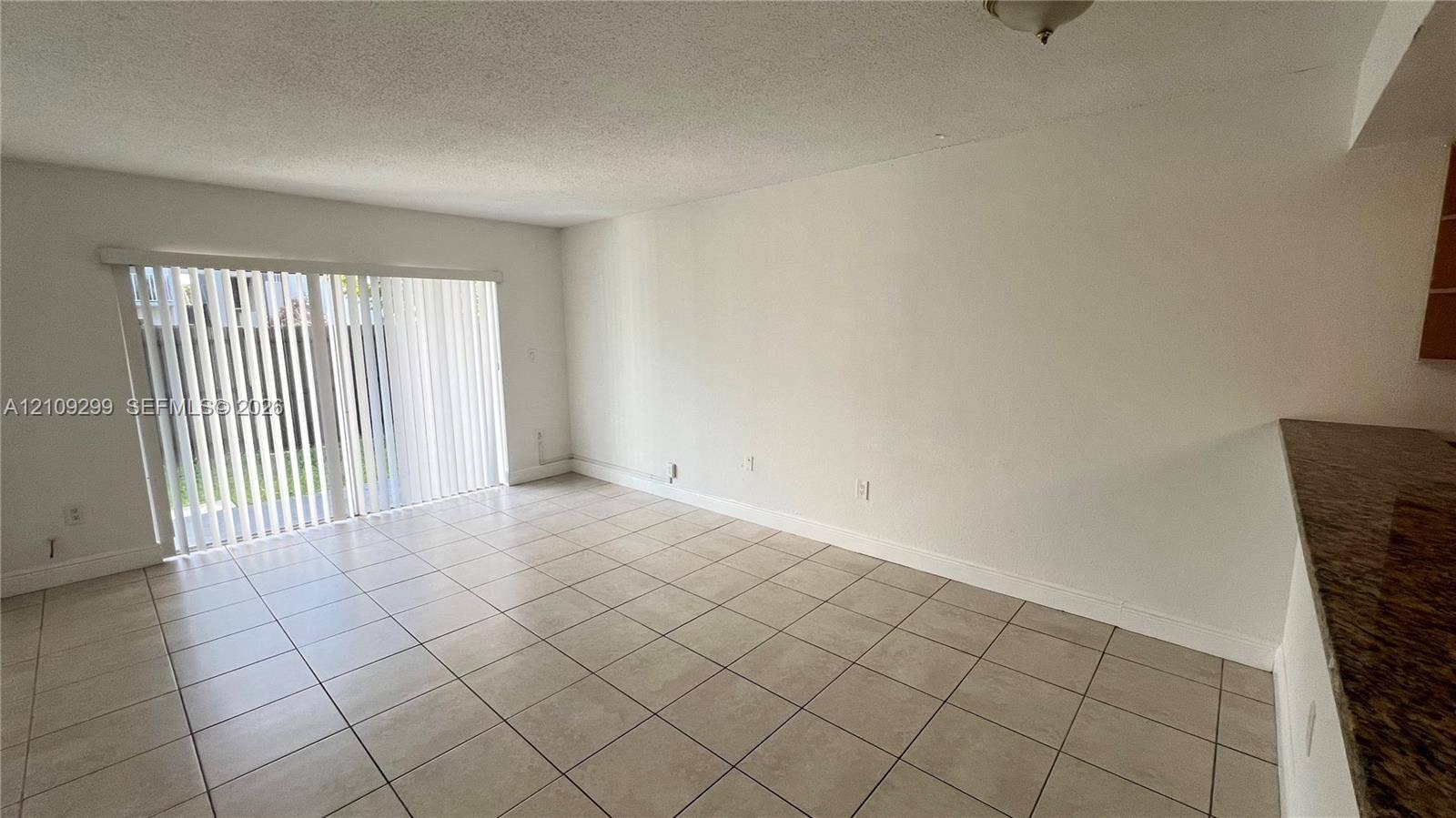 4810 NW 79 Avenue, #107, Doral, Doral, FL 33166 Interior space featuring light-toned ceramic tile flooring, sliding glass door with vertical blinds, and stone-finish countertop