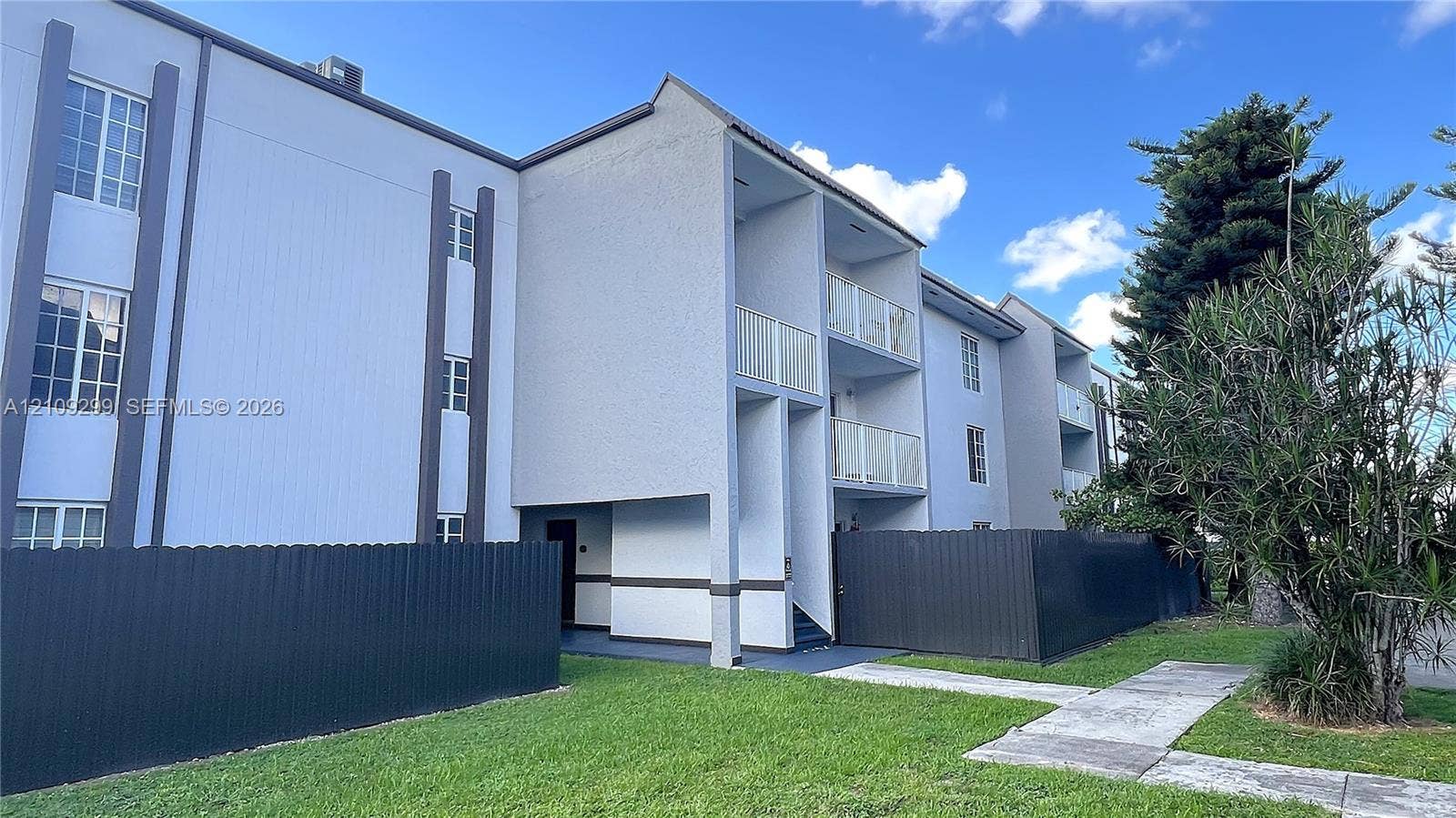 4810 NW 79 Avenue, #107, Doral, Doral, FL 33166 Multi-story exterior featuring a light-toned stucco faade, private elevated balconies with metal railings, and dark-finished metal privacy fencing