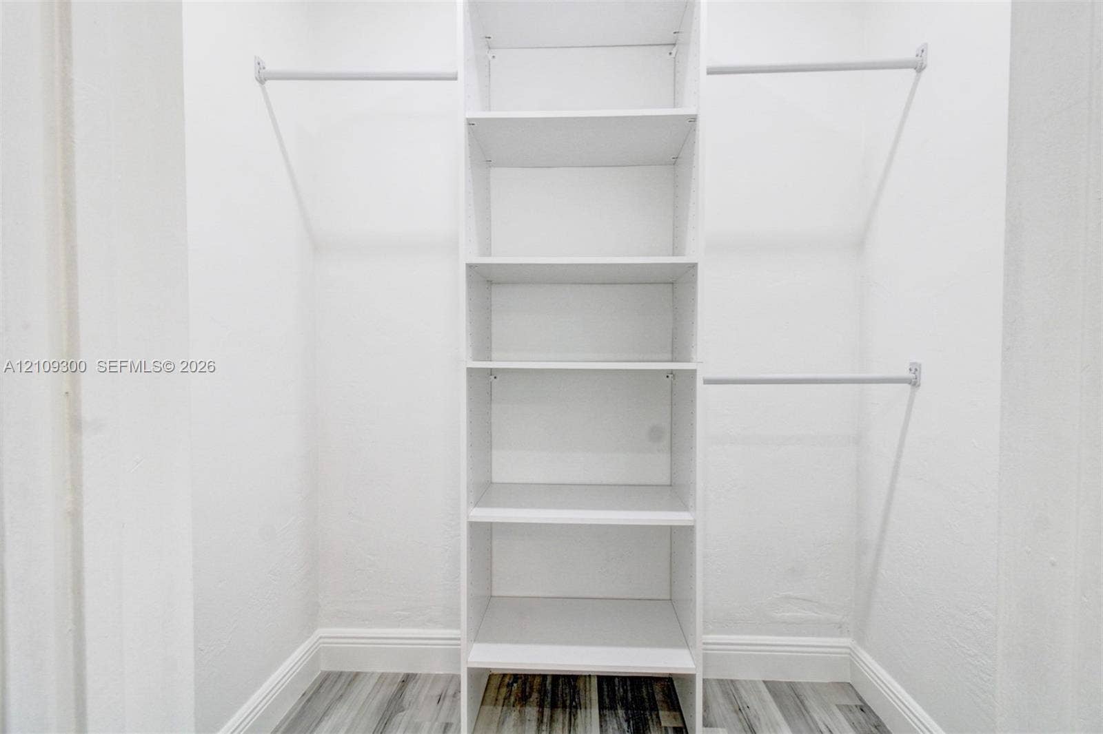 Walk-in closet featuring white built-in shelving, dual-level garment rods, and wood-finish flooring