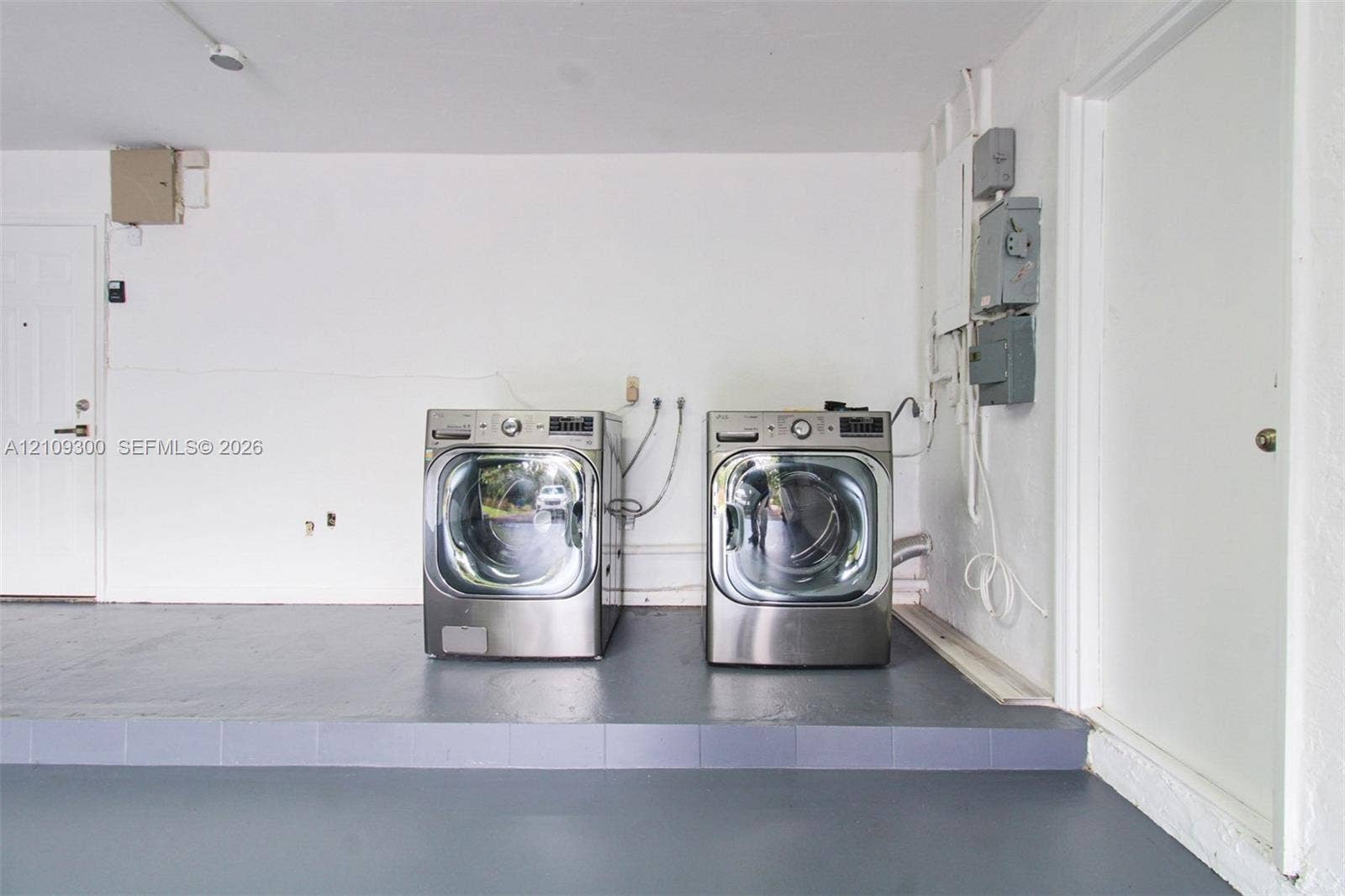 Dedicated laundry area featuring a raised platform, painted concrete flooring, and multiple solid-core doors
