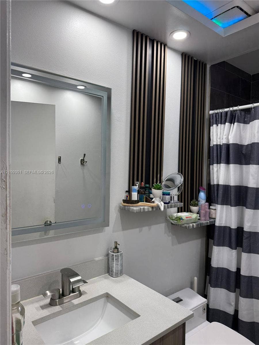 7680 SW 153rd Court, #204, Miami, Miami, FL 33193 Bathroom featuring a vanity with a stone-surface countertop, an integrated rectangular sink, a polished metal faucet, a backlit rectangular mirror, and decorative wall-mounted acoustic-style slats with built-in stone-finish shelving