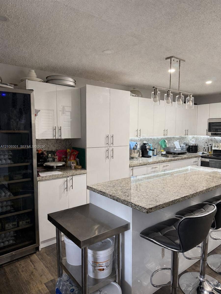 7680 SW 153rd Court, #204, Miami, Miami, FL 33193 Kitchen featuring glossy white cabinetry, stone countertops, a central island with an integrated breakfast bar, a built-in wine refrigerator, and a linear multi-light pendant fixture
