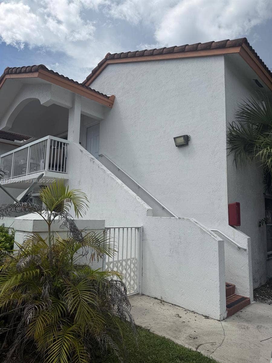 7680 SW 153rd Court, #204, Miami, Miami, FL 33193 Stucco exterior featuring a tiled roof, upper-level balcony with metal railing, and concrete staircase with integrated handrail