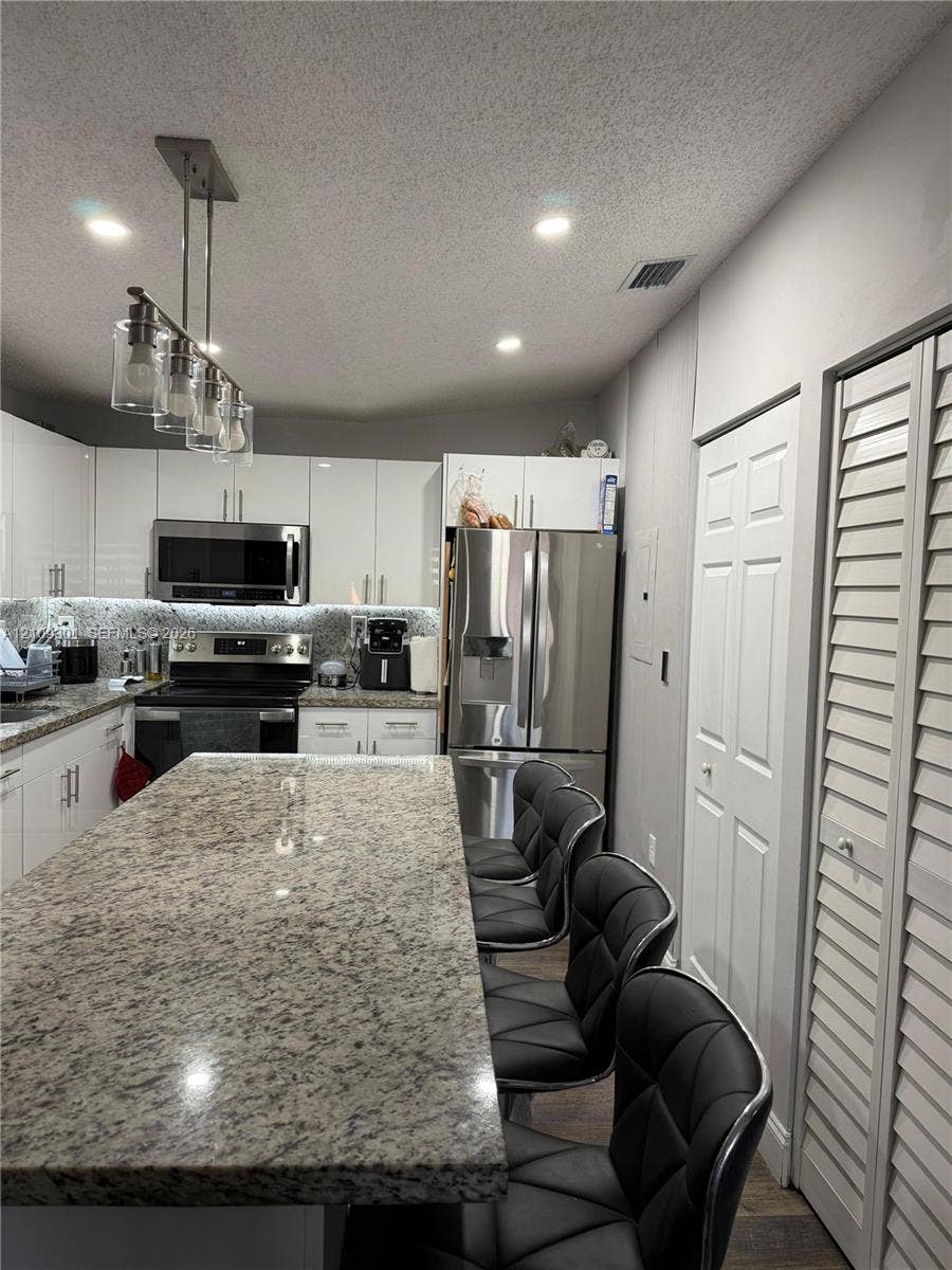7680 SW 153rd Court, #204, Miami, Miami, FL 33193 Kitchen featuring a large central island with stone countertop, gloss-finish cabinetry, stainless steel appliances, and a multi-light pendant fixture