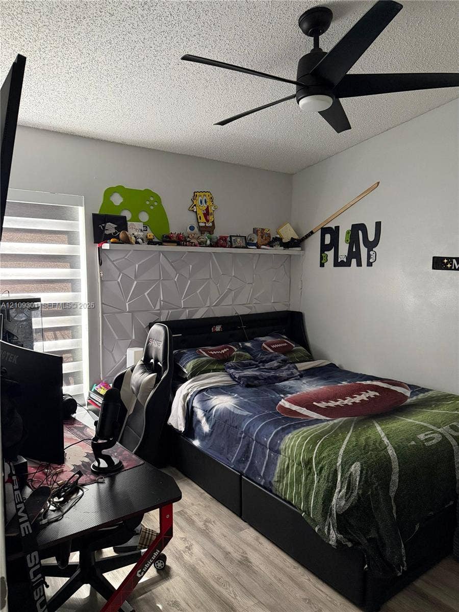 7680 SW 153rd Court, #204, Miami, Miami, FL 33193 Textured geometric wall paneling with a floating shelf, matte black ceiling fan, wood-finish flooring, and horizontal layered blinds