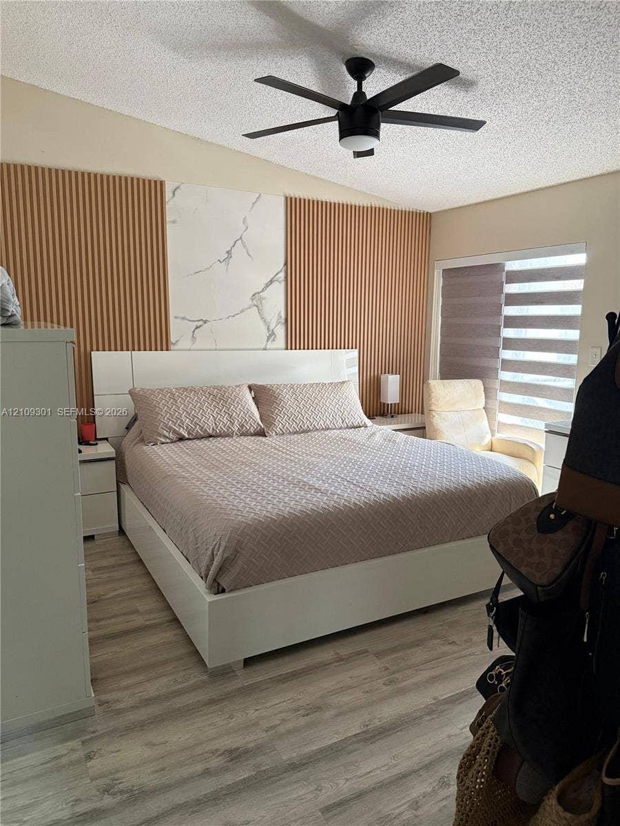 7680 SW 153rd Court, #204, Miami, Miami, FL 33193 Accent wall featuring vertical slatted panels and a central stone-patterned tile inlay, wood-finish flooring, and a ceiling-mounted fan with integrated lighting