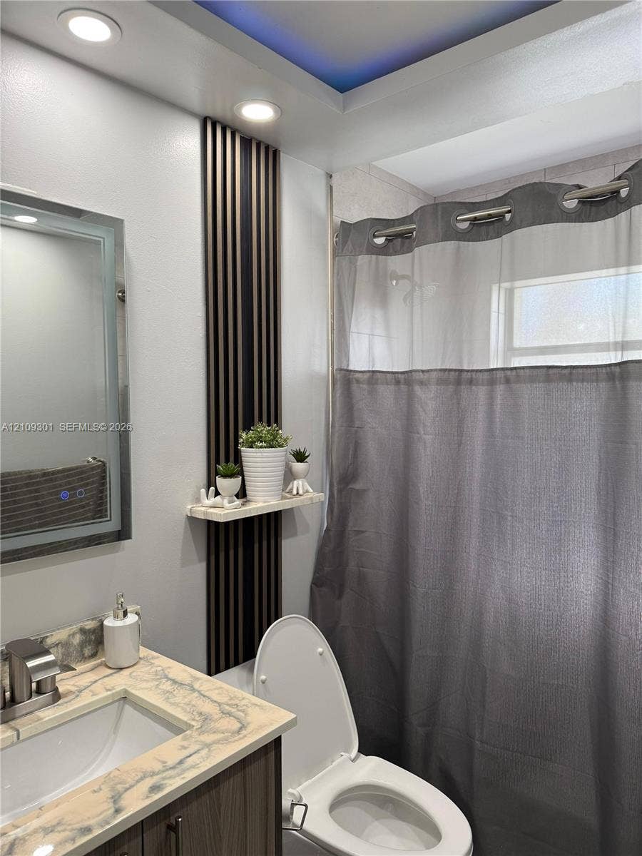 7680 SW 153rd Court, #204, Miami, Miami, FL 33193 Bathroom featuring a stone-look countertop with an integrated sink, vertical slat accent wall paneling with a floating shelf, recessed ceiling lighting, and a tray ceiling detail with integrated color-accent lighting