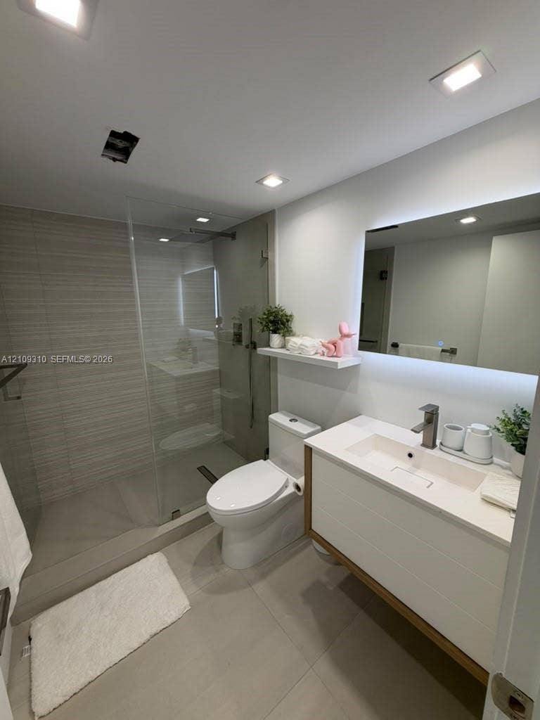 Walk-in shower with horizontal tile surround and glass partition, floating vanity featuring a rectangular integrated sink, white countertop, and LED-backlit mirror