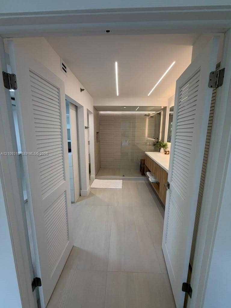 Bathroom featuring dual louvered doors, recessed linear ceiling lighting, floating wood-finish vanity with countertop, and a walk-in glass-enclosed shower with tile surround