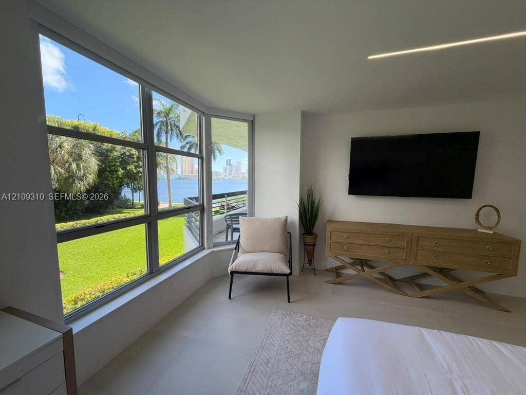 Floor-to-ceiling windows featuring waterfront scenery, neutral tile flooring, recessed linear lighting, and wall-mounted television console