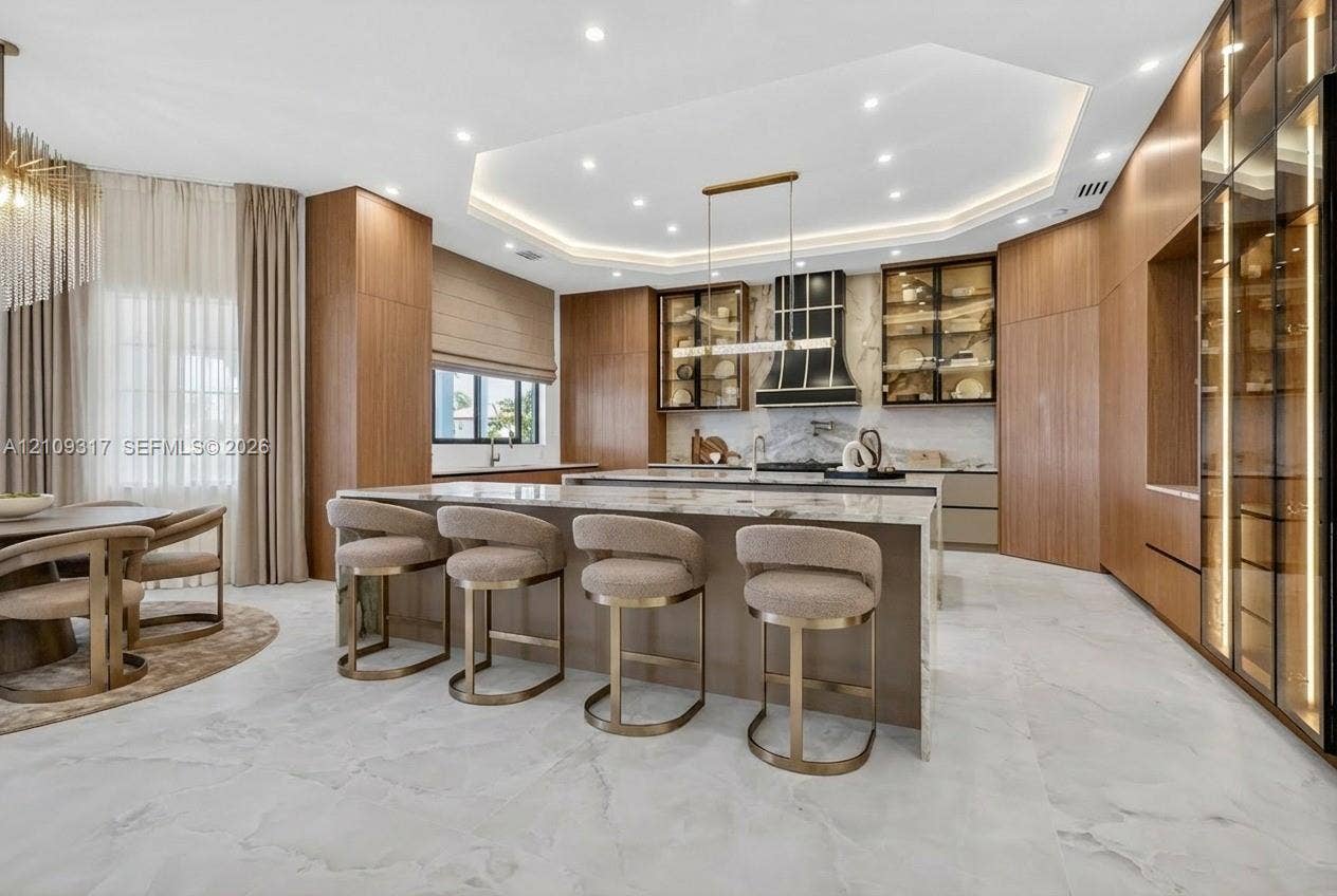 Custom kitchen featuring wood-finish cabinetry, stone countertops, integrated lighting, a stone-patterned island, and large-format flooring