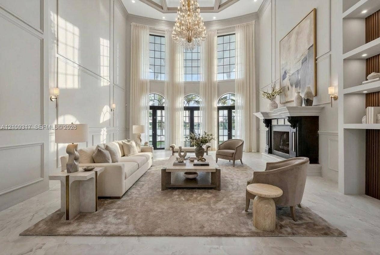 Double-height living area featuring floor-to-ceiling windows, wainscoting wall detailing, a fireplace with a traditional mantel, and built-in shelving
