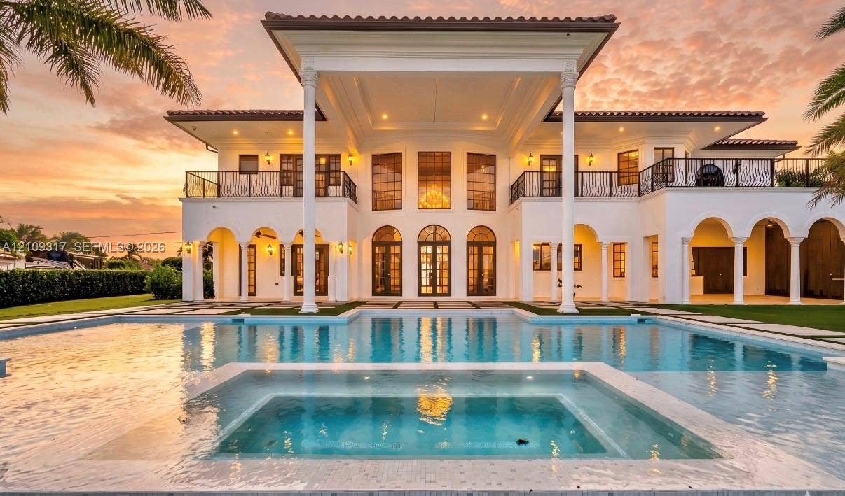 Two-story Mediterranean estate featuring arched colonnades, a second-level wrought iron balcony, custom multi-pane fenestration, and a ground-level swimming pool with an integrated spa