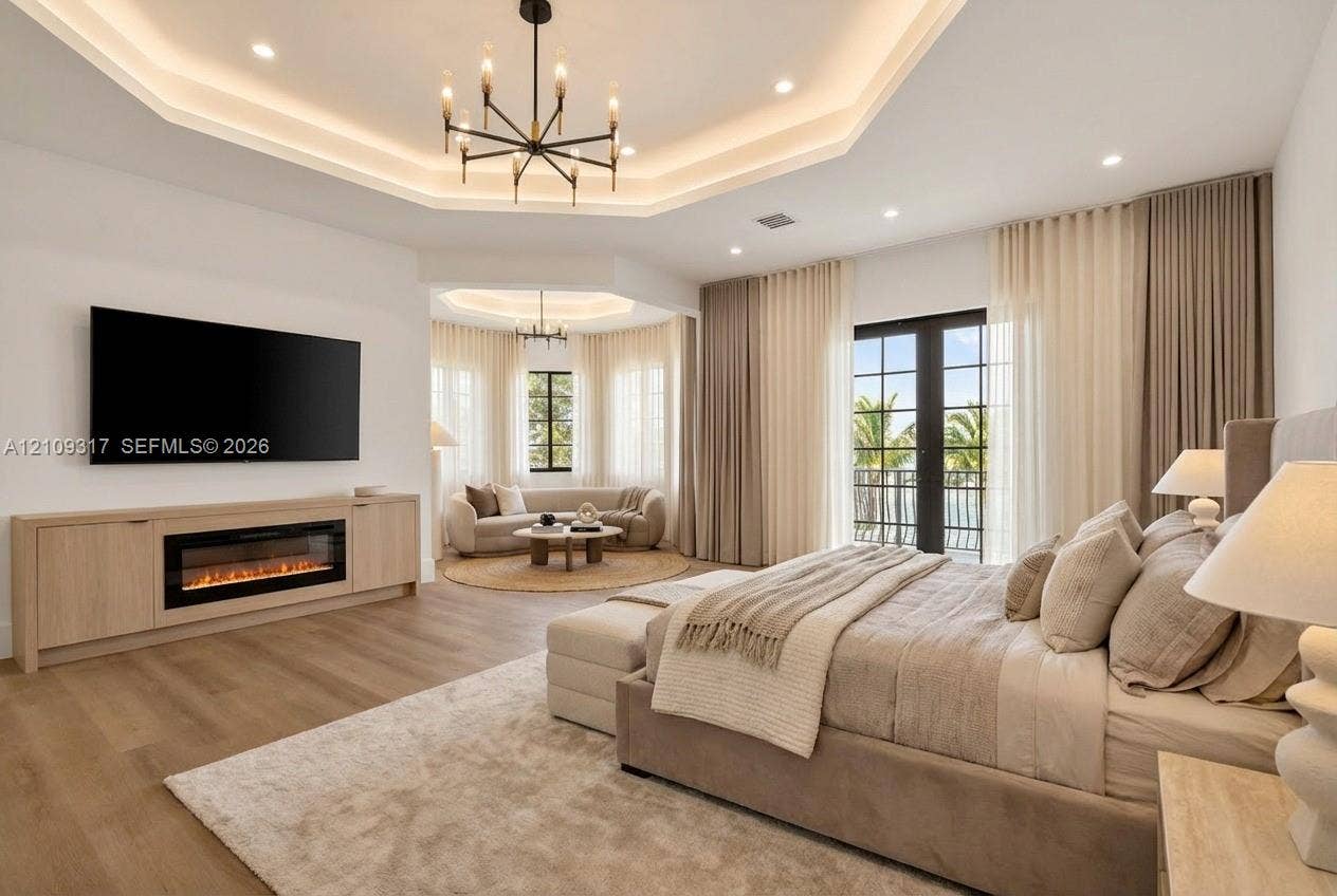 Tray ceiling with recessed lighting, built-in cabinetry featuring an integrated electric fireplace, wood-finish flooring, and black-framed French doors