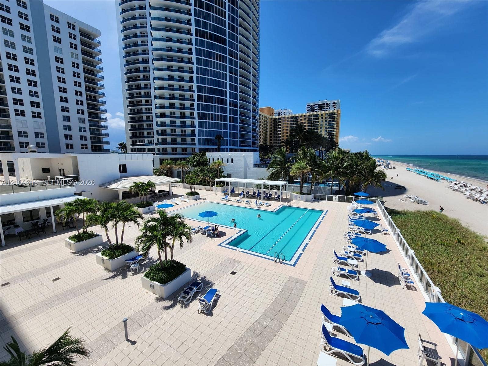 2751 S Ocean Drive, #1608N, Hollywood, FL 33019 Expansive paved pool deck featuring a swimming pool, integrated landscaping with palms, and direct beachfront access
