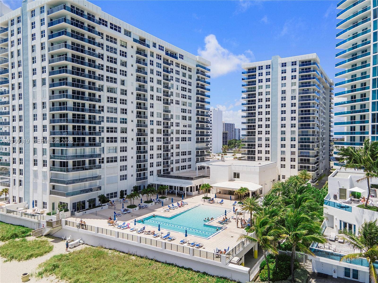 2751 S Ocean Drive, #1608N, Hollywood, FL 33019 High-rise residential complex featuring a swimming pool, tiled sundeck, palm tree landscaping, and direct access to sandy beach terrain