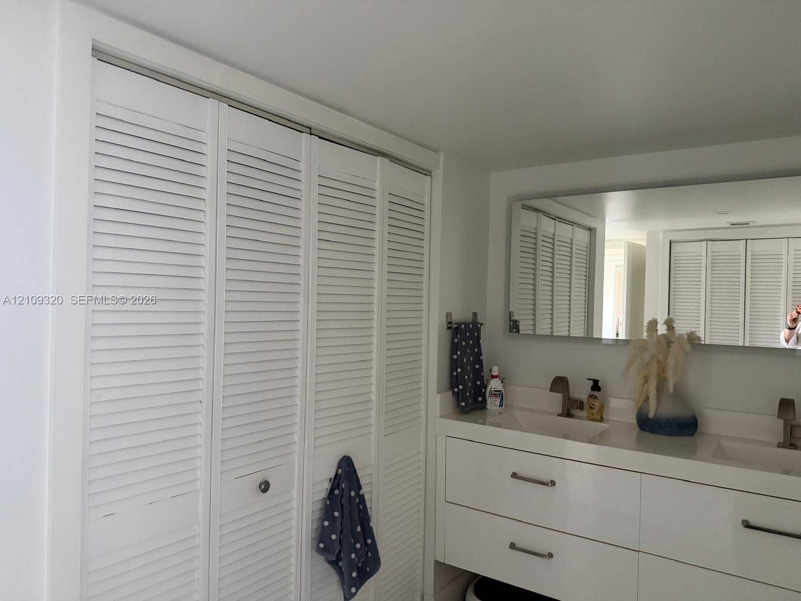 Floating vanity with dual rectangular sinks, white cabinetry, quartz countertop, polished metal faucets, and floor-to-ceiling louvered closet doors