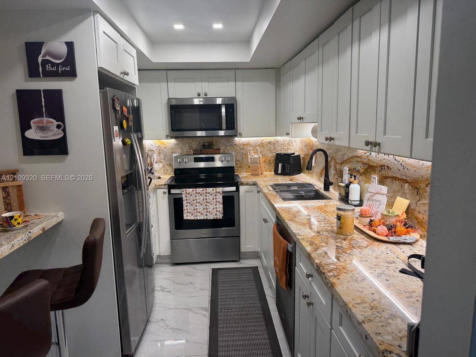 Kitchen featuring light-toned shaker cabinetry, stone countertops with an integrated backsplash, stainless steel appliances, and large-format tile flooring