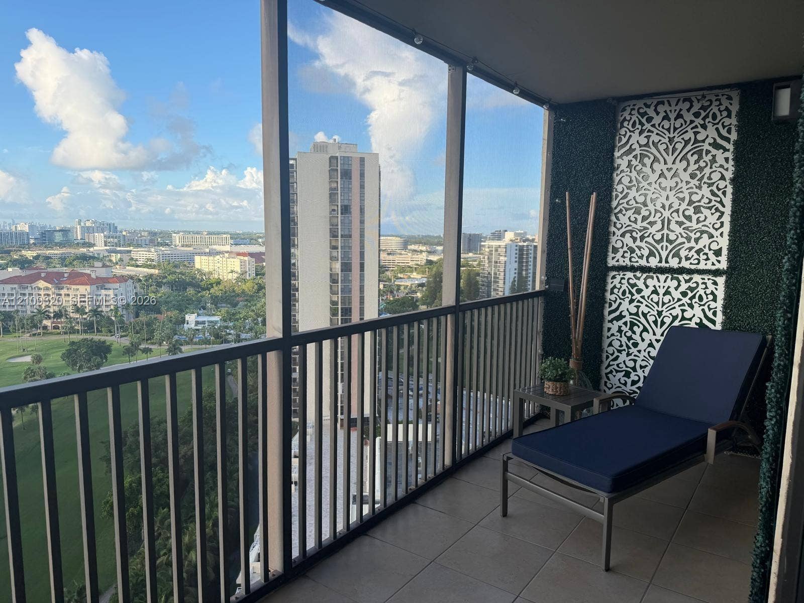 Screened balcony featuring dark metal railings and tile flooring with panoramic scenery of a golf course and a city skyline